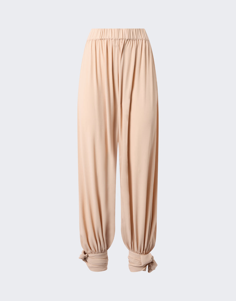 Frontal view — Noor Maxi Pants: peach crepe de chine pants hang, draping wide balloon-shaped legs from elastic low-rise waistband, tapering to tied ankle cuffs on plain background.
