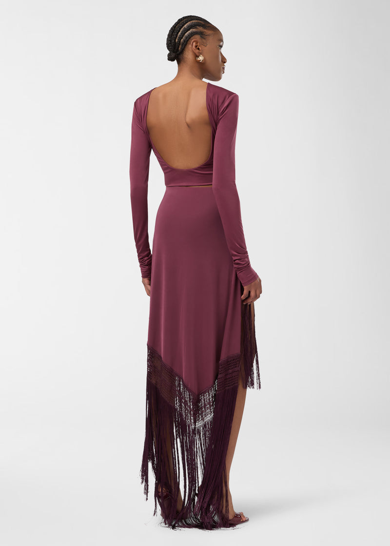 Rear view — Model wearing Lia Top: cropped, long-sleeve, high-neck jersey top in rouge noir with a deep open scoop back, shown with a fringe midi skirt.