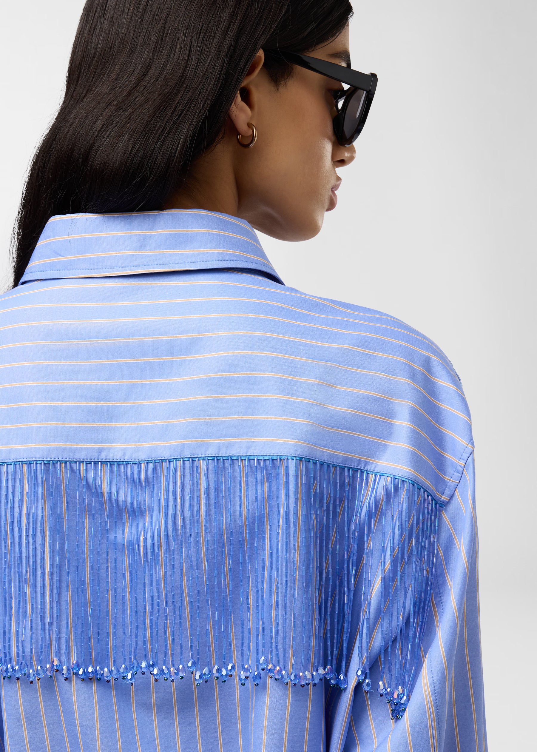 Rear view — Miley Shirt: model wearing light-blue and saffron maxi-striped cotton-poplin shirt showcasing bejeweled fringe trim hanging from back yoke seam beneath a pointed collar.
