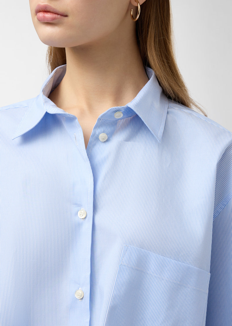 Frontal view — Cropped Georgiana Shirt: close-up of model wearing light-blue-and-white micro-striped cotton poplin, showing pointed collar, button placket, chest patch pocket and dropped shoulder.