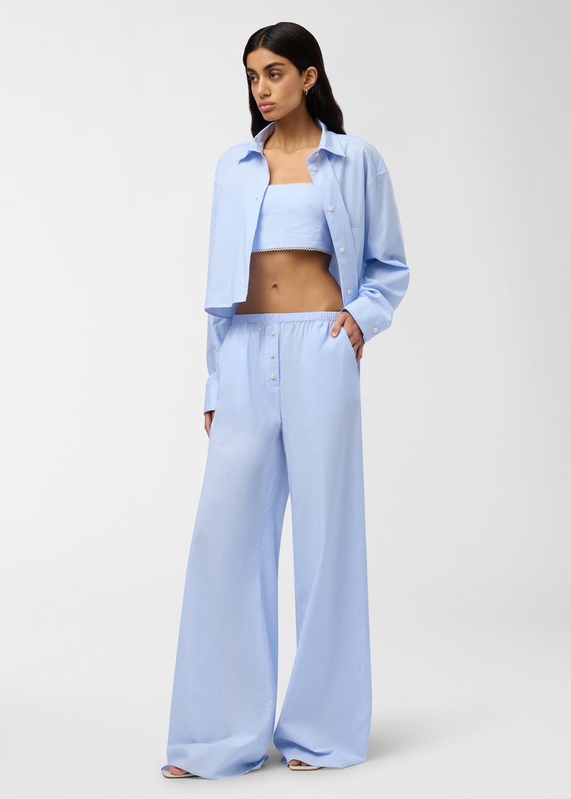 Frontal view — Model wearing Carrie Top, a light-blue micro-striped cropped bralette with spaghetti straps and delicate lace hem, styled under an open matching shirt and wide-leg pants in studio.