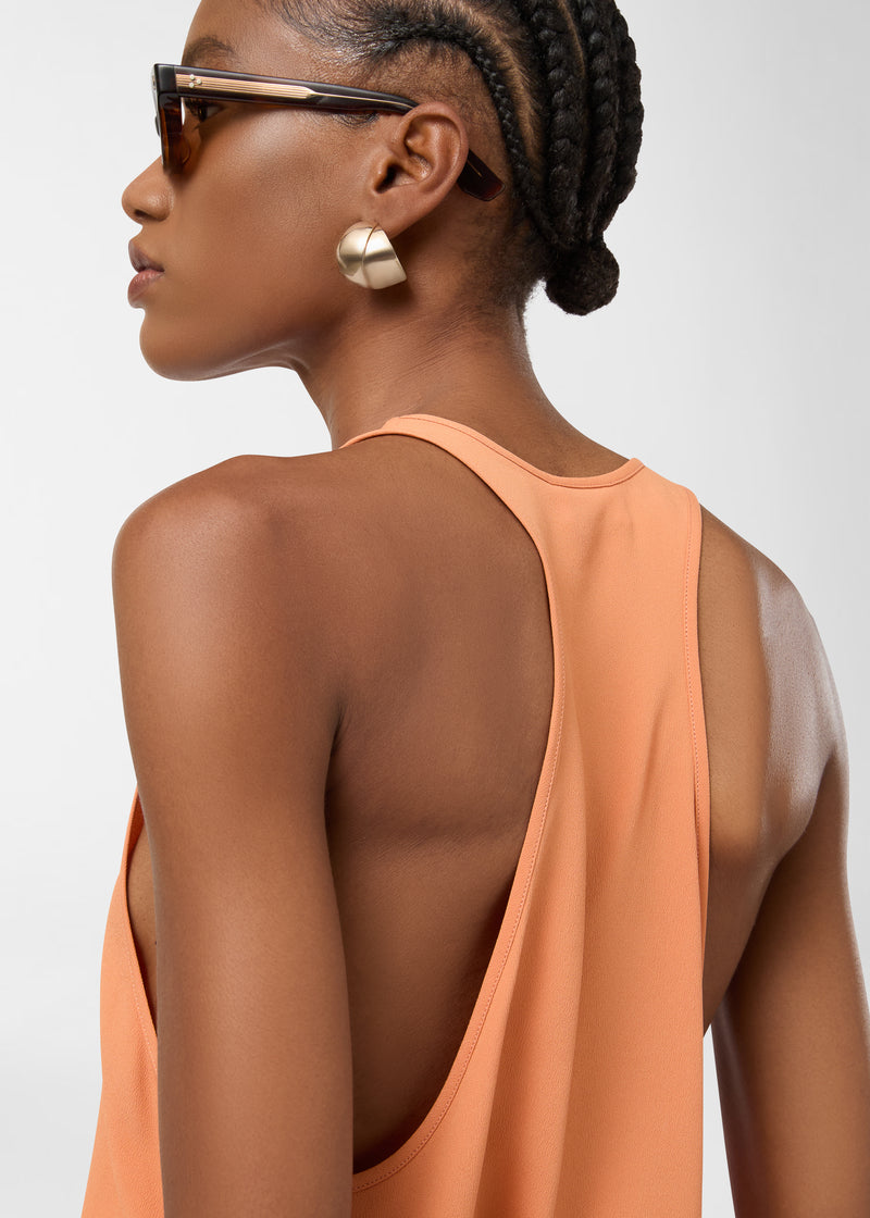 Rear view: Model wearing Pura Top in tangerine crepe de chine, showing racerback and scooped neckline framing shoulders, fabric draping fluidly down the bodice.