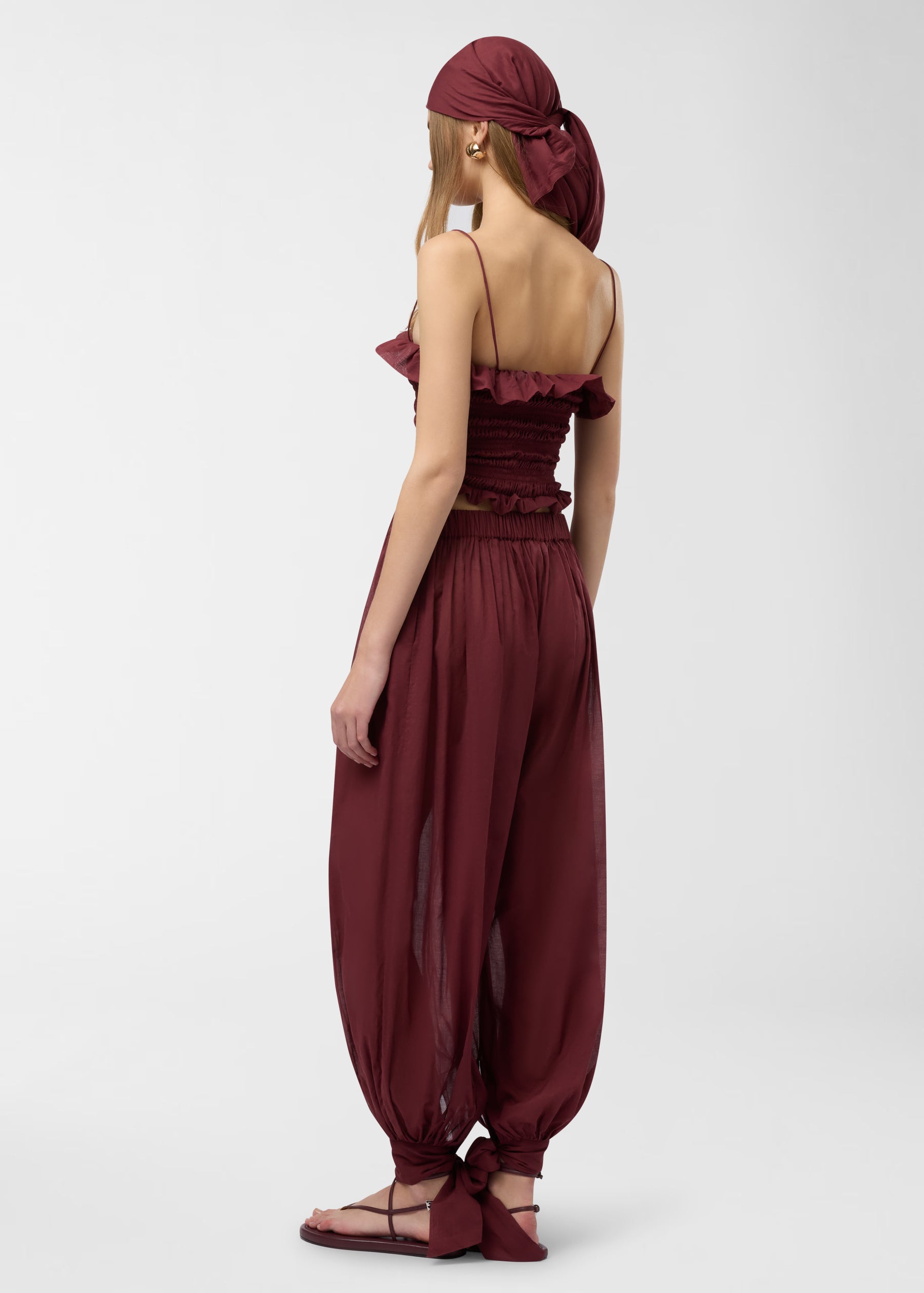 Rear view, Suri Top worn by model: rouge noir smocked tube top with spaghetti straps and undulated ruffle at chest seam; hugs silhouette, studio background.