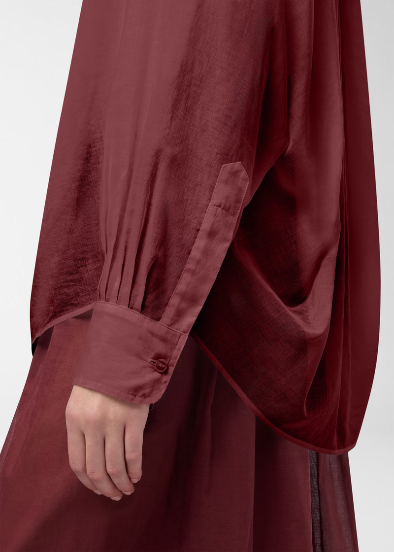 Detail view — Rania Shirt: oversized rouge noir cotton muslin sleeve draping over hip, pleated cuff fastened with a single button, semi-sheer lightweight texture and soft folds.
