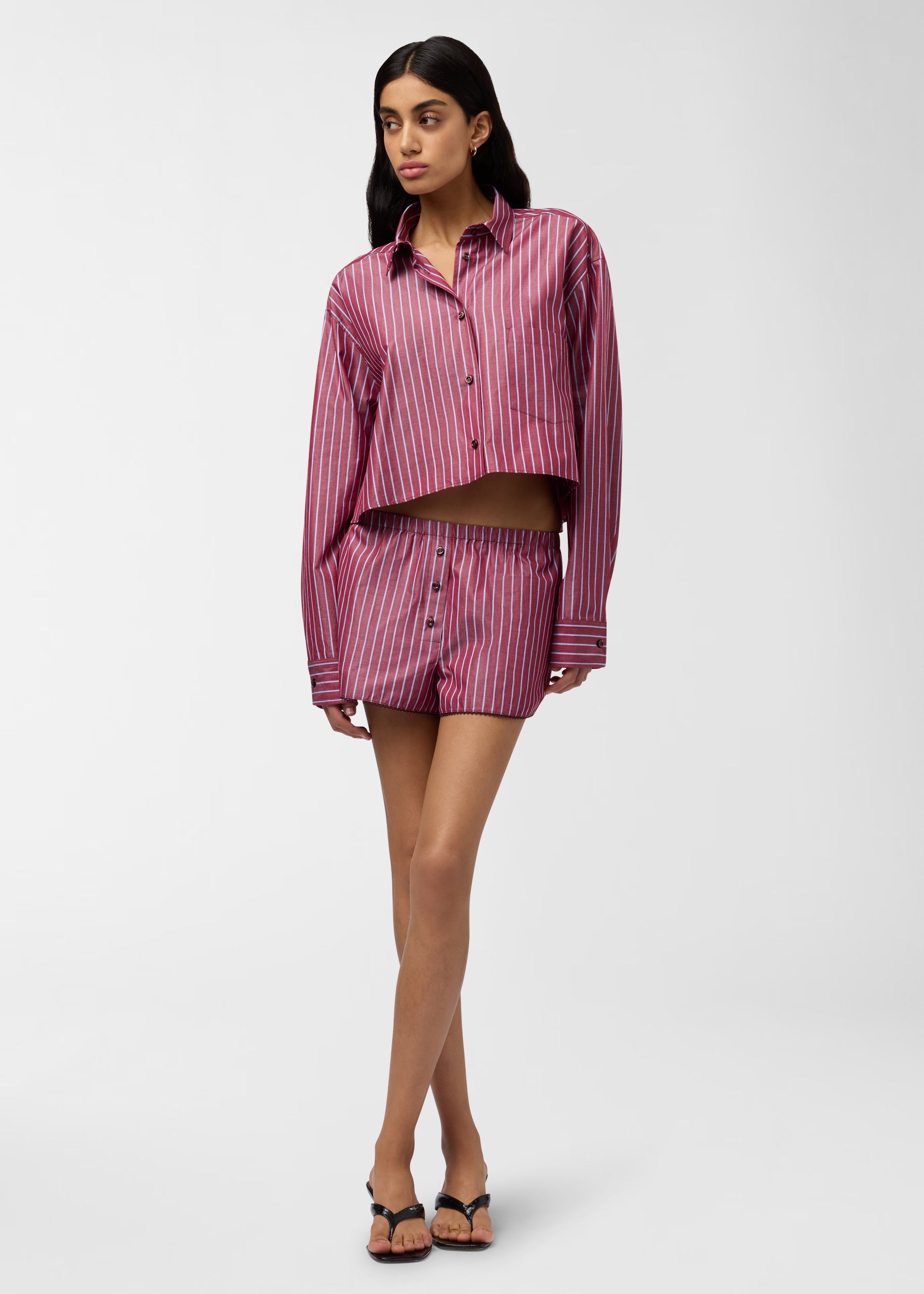 Frontal view — Model wearing Arabella Set: cropped long-sleeve button shirt and elastic-waist shorts in rouge noir with light-blue vertical stripes, standing on white background.