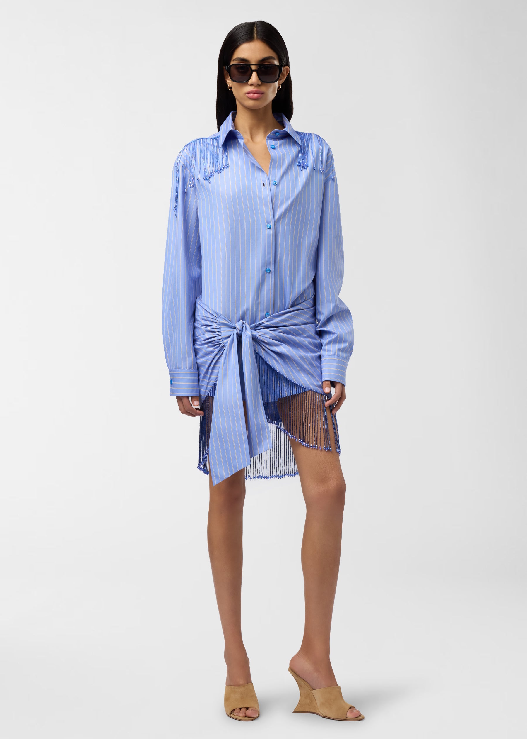 Frontal view — Dolly Pareo: light blue maxi-striped cotton wrap tied at waist with draped pleats and knotted front, bejeweled fringe hem, modeled on standing woman.